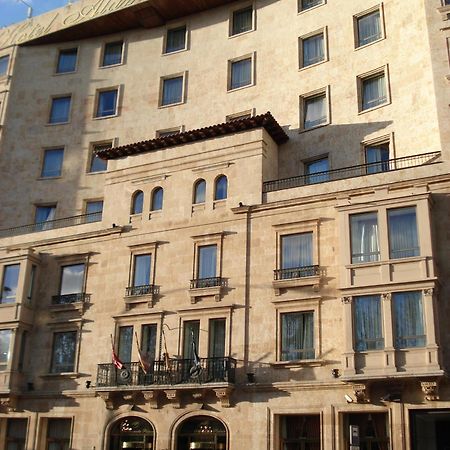 ホテル オテル アラメーダ パラス サラマンカ エクステリア 写真 The photo depicts a building with a stone facade that features a mix of architectural designs. The lower section includes several large windows framed by decorative elements, with balconies that have railings. There are also flags visible at the entr
