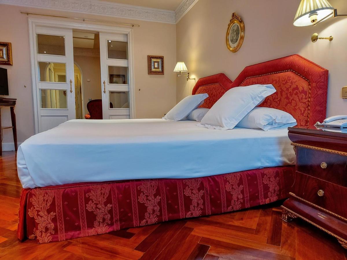 ホテル オテル アラメーダ パラス サラマンカ エクステリア 写真 The photo depicts a cozy hotel room featuring a double bed with a red and gold patterned bed skirt. The bed's headboard is also red and has an elegant design. Pillows are neatly arranged on the bed. There is wooden flooring visible, and the room has 