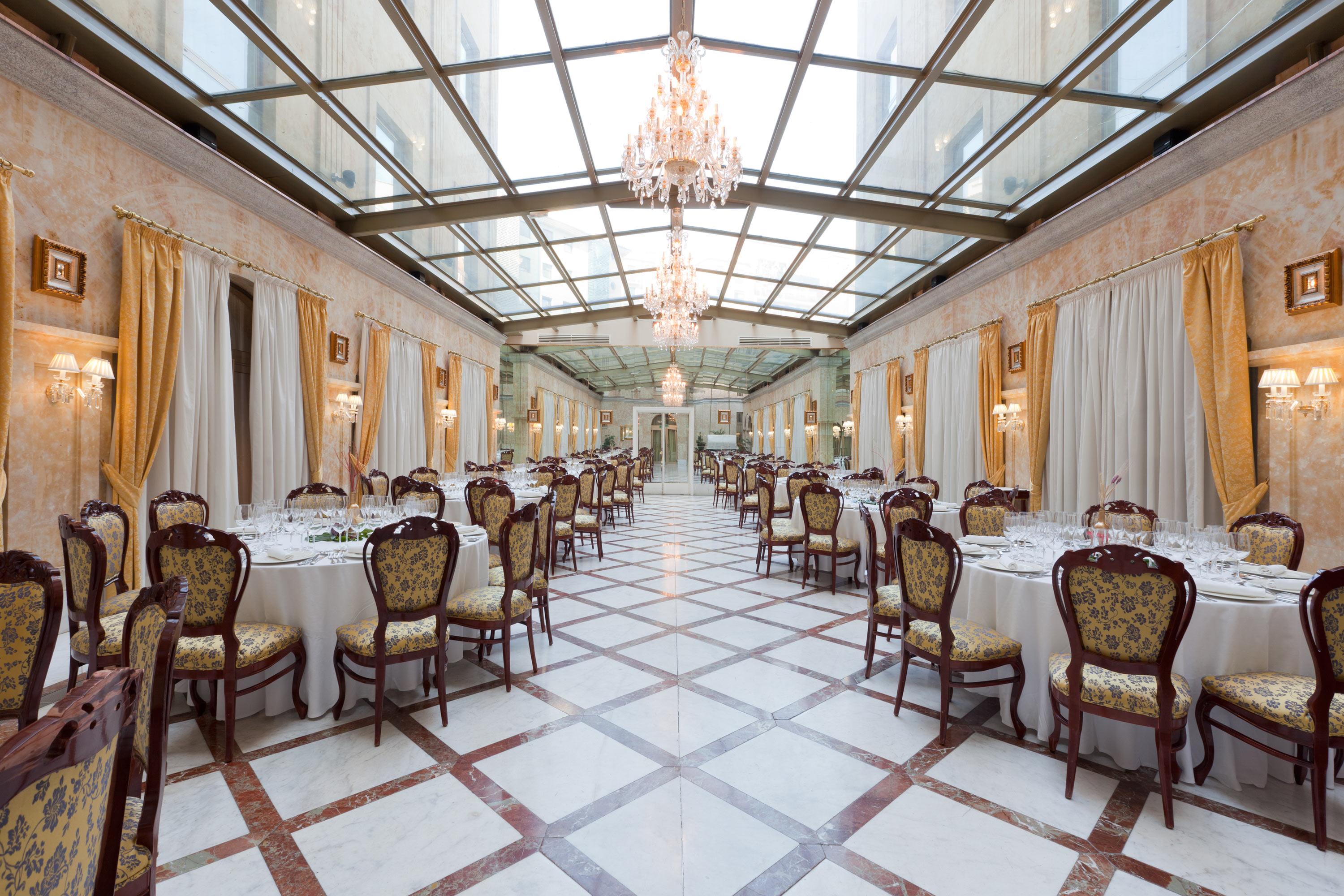 ホテル オテル アラメーダ パラス サラマンカ エクステリア 写真 The photo shows the interior of an elegantly designed restaurant. It features a long dining area with several round tables, each set with white tablecloths and fine dining tableware. The chairs are ornate, likely upholstered in a rich fabric with a c