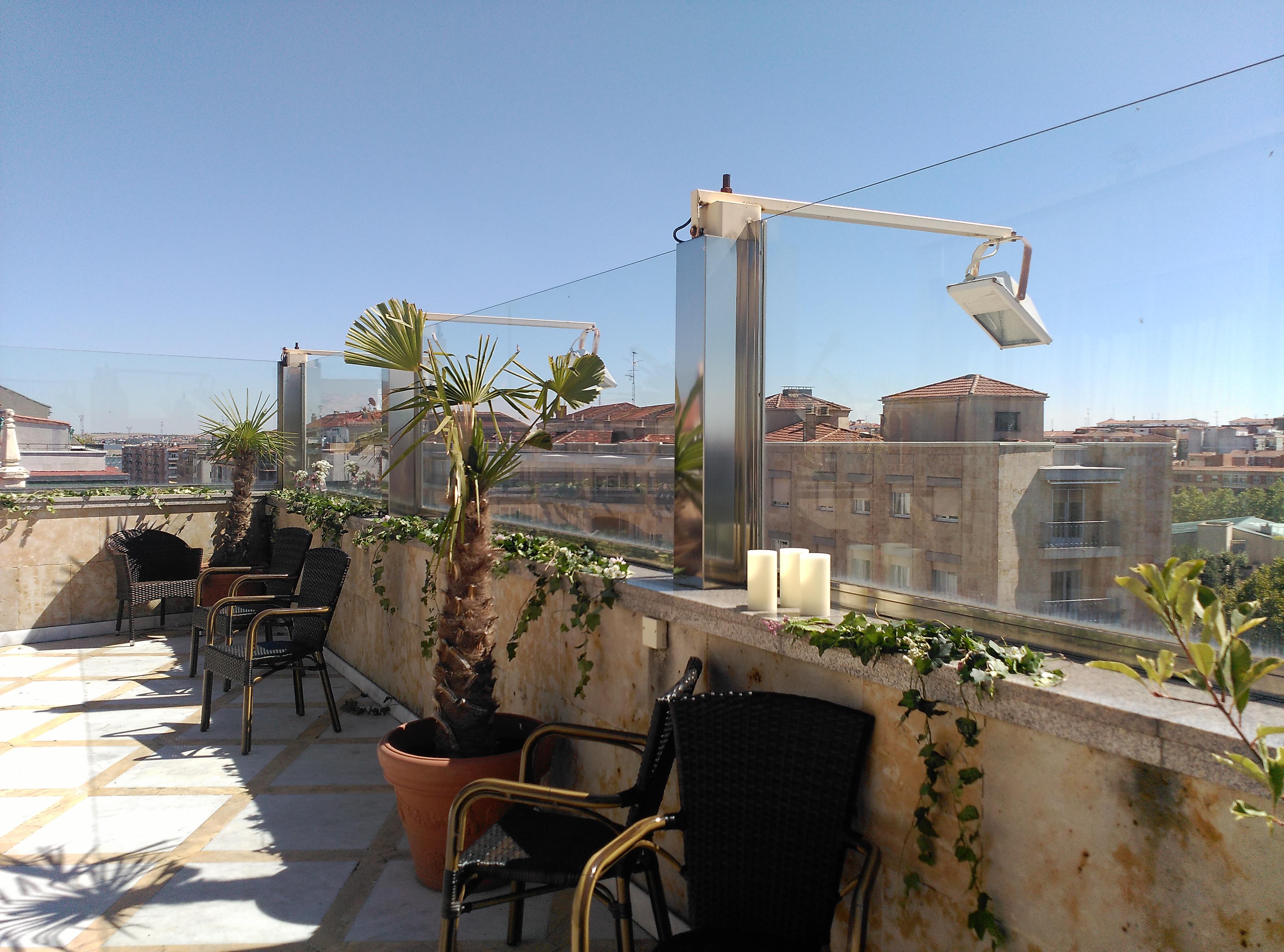 ホテル オテル アラメーダ パラス サラマンカ エクステリア 写真 The photo shows a rooftop terrace featuring a sunny environment. There are several chairs arranged on the terrace, along with potted plants, including palm-like greenery. The terrace has clear glass panels that provide a view of the surrounding build