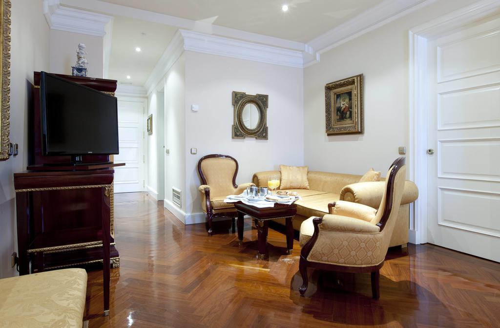 ホテル オテル アラメーダ パラス サラマンカ エクステリア 写真 The photo depicts a well-furnished living room. It features a cream-colored sofa with elegant armchairs around a dark wooden coffee table. A flat-screen television is mounted on a polished wooden unit. The floor is made of hardwood, contributing to t