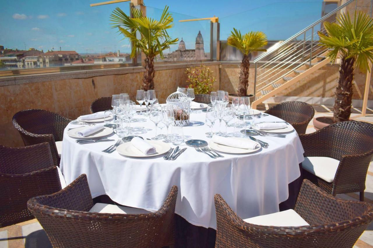 ホテル オテル アラメーダ パラス サラマンカ エクステリア 写真 The photo shows a round dining table set for a meal, covered with a white tablecloth. The table is surrounded by wicker chairs and features several glassware items, including wine glasses and water glasses, as well as cutlery and napkins neatly arran